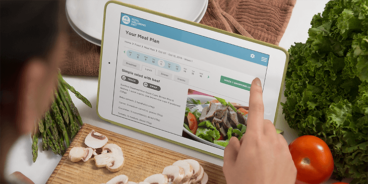 woman looking at total wellbeing diet meal plans on  ipad while cooking