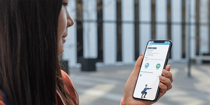 woman in hoodie outside checking her exercise plan on an iphone
