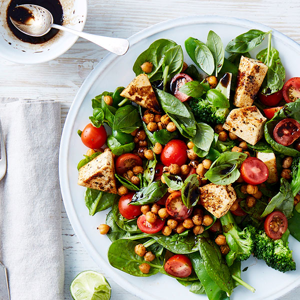 Plate with a simple salad of roasted chickpeas, baby spinach, halved baby tomatoes, broccoli and fried haloumi