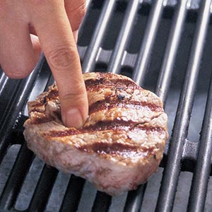 checking the firmness of a steak on a grill