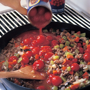 adding tomatoes to frying pan with cooked mince and vegetables