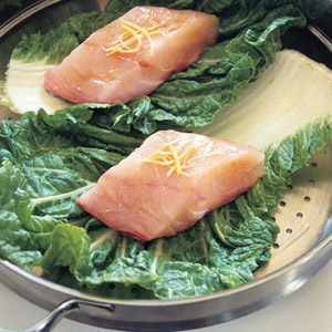 pieces of fish in a steamer on a layer of cabbage leaves