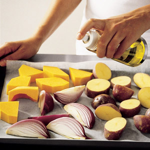 spraying pieces of red onion and pumpkin on a baking tray