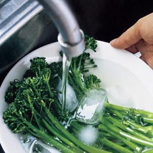 blanching broccoli with ice and water in a colander under the tap