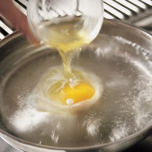 pouring an egg from a small bowl into a frying pan with water