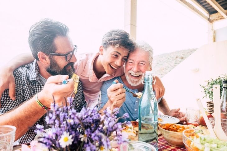 Three happy males sitting around a table and eating healthy food.
