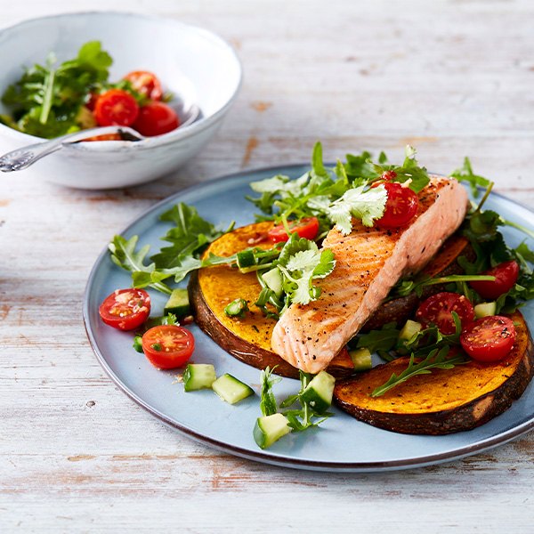 Plate of baked salmon and pumpkin with slices of cucumber, tomato and coriander
