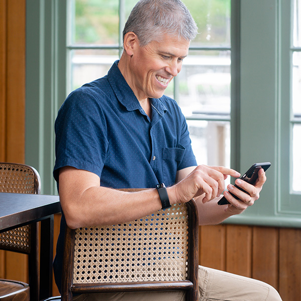 Member Terry in a blue button up shirt, sitting at a table and using the online program on his phone.