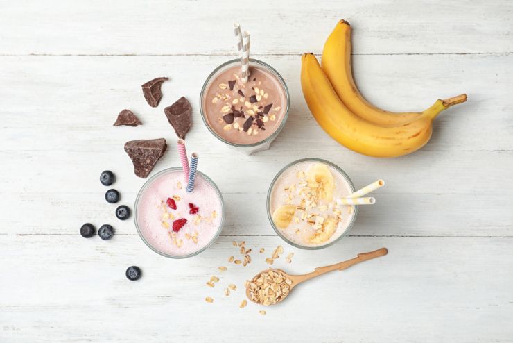 Chocolate, vanilla and banana meal replacement shakes in glasses with bananas and oats and blueberries.