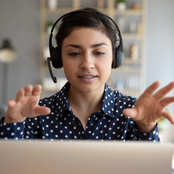 Close up of woman with a headset making hand gestures at the camera of her laptop computer