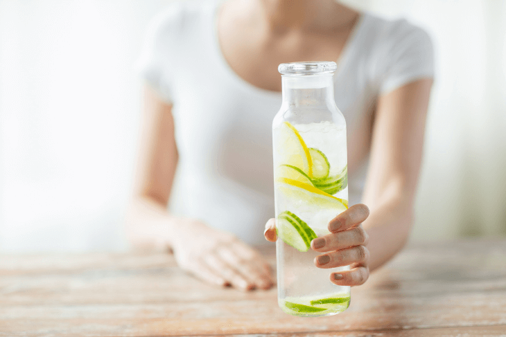 Woman holding glass water bottle with  sliced cucumber and lemon