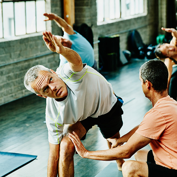 Middle aged man in yoga class getting assistance from a trainer.